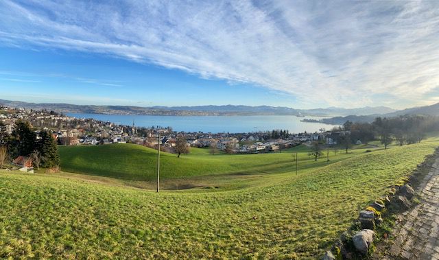 Aussicht vom Heimetli mit Herz über grüne Wiesen, weiter unten ist der See und im Hintergrund die Berge zu sehen.