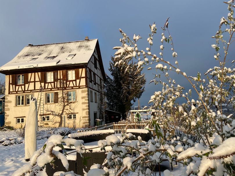 Es liegt Schnee. Das Haus ist aus einer Distanz von ca. 50 Meter fotografiert. Das dreistöckige Haus ist aus Stein gebaut und weist oben eine Riegelbaustruktur auf. Es hat ein Satteldach.
